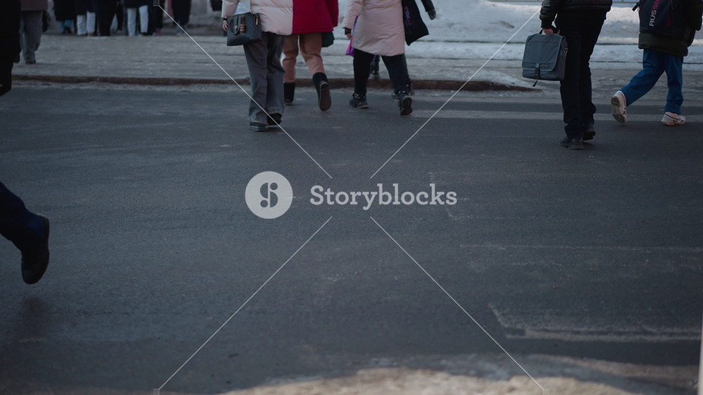 back view pedestrians in winter coats walking past sign post on city street, carrying handbag, stepping from slushy curb onto wet asphalt