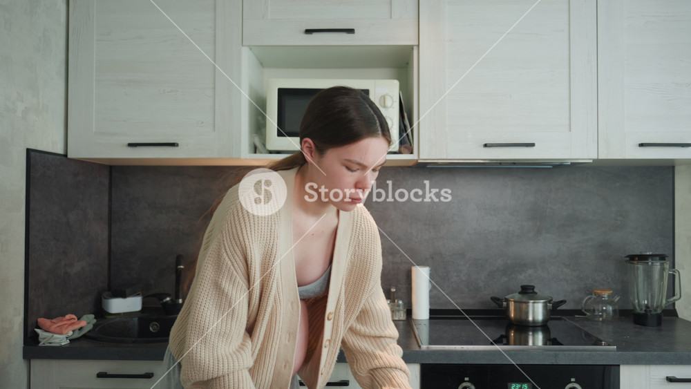 Expectant woman gazes at stove peacefully. Pregnant woman in comfortable sweater observes stove calmly. Expectant woman relaxingly watches