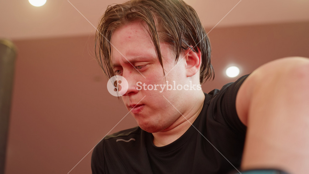 Male fighter breathing heavily after sparring in gym, face flushed with effort, sweat visible, wearing black sportswear, showing exhaustion