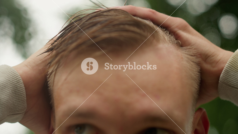 wet hair inspection rainy park caucasian man, closeup checking strands and scalp with worried gaze, droplets on forehead, casual commuter