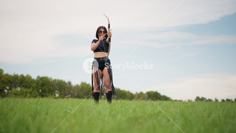 solitary archer woman standing in field surveying horizon, leather fringe costume and bow at rest cinematic wide shot with open sky, distant