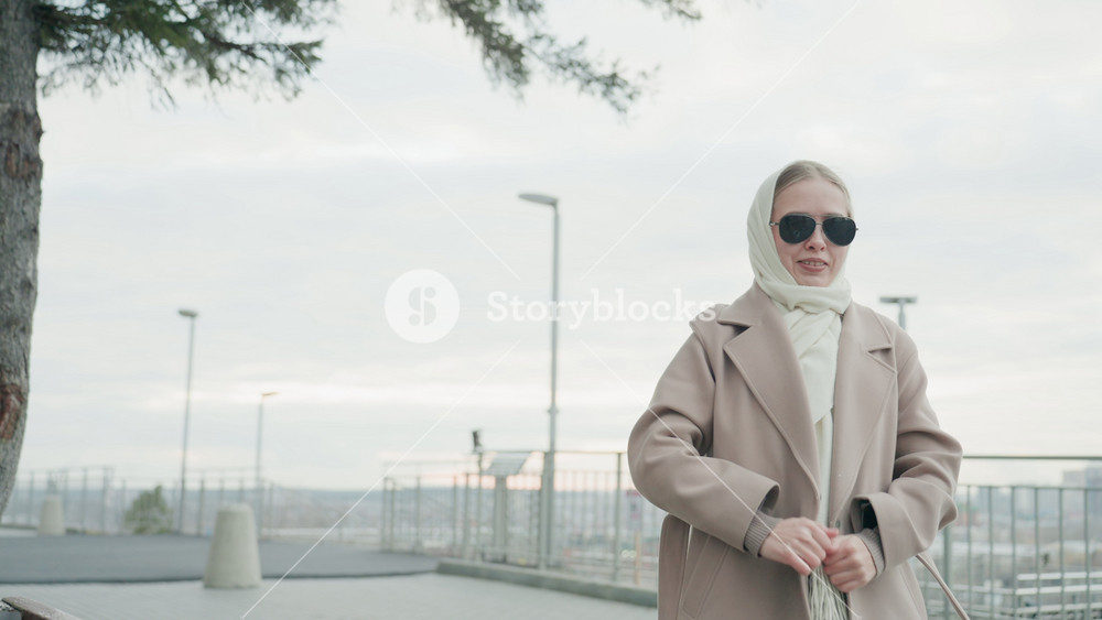 Calm lady with scarf by railing. Thoughtful woman smoothing her scarf and coat quietly. Contemplative woman adjusting her scarf and coat