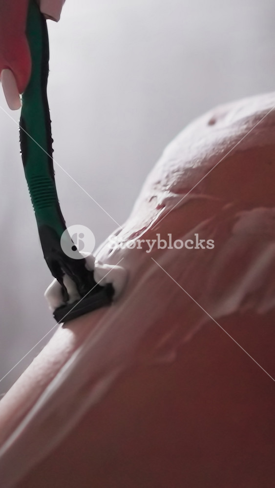 Woman removes leg skin hair with razor in shower closeup. Slim lady shaves body with sharp blade in bathroom. Woman does beauty procedure at