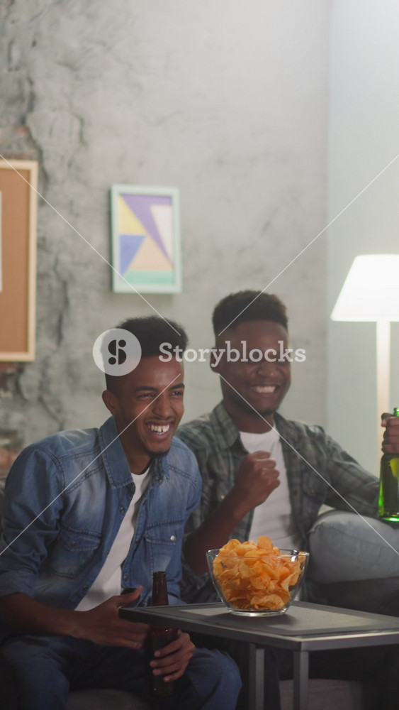Joyful emotional friendly colleagues excited of goal shoot watching match via TV in apartment slow motion. Sports fans during football team