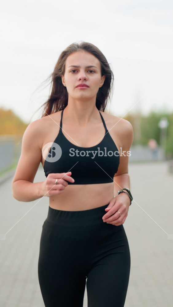 Close-up view of woman jogging in black fitness wear in park with benches and trees in background, active lifestyle, fitness, and healthy