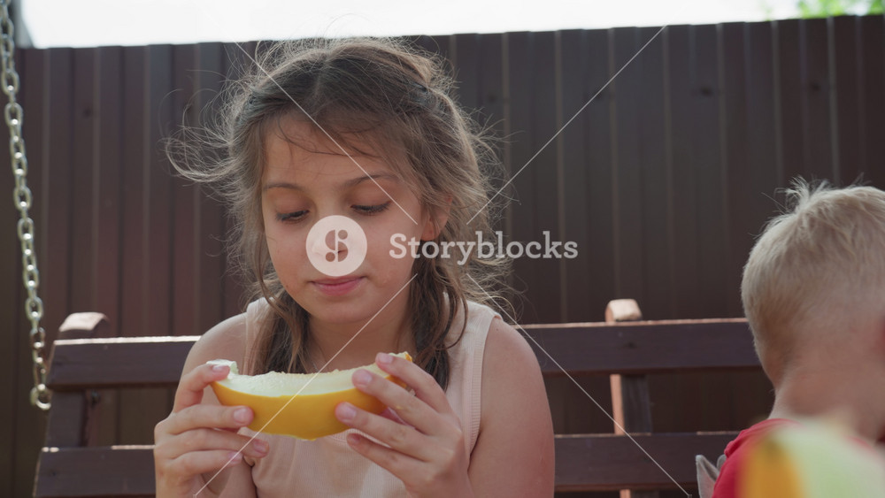 Children Sharing And Observing Food, Child And Sibling Enjoy Snack As Girl Studies Melon Slice Attentively, Young Girl Watches Fruit