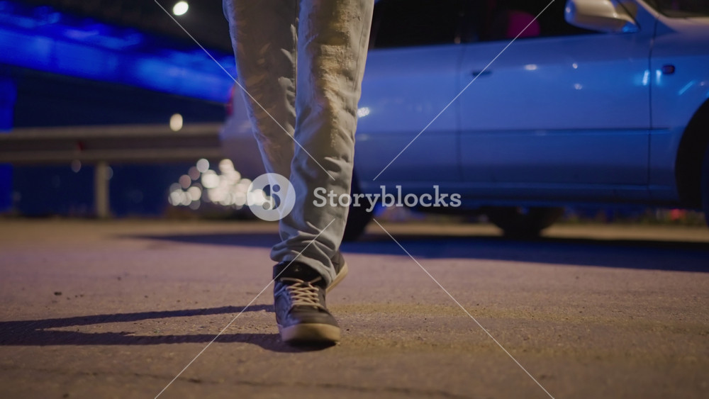 night curb closeup underbody foot near open door, adult rideshare driver in sneakers and jeans pausing beside silver sedan, blue neon and