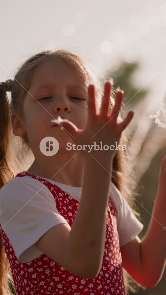 Little girl puts piece of cotton candy into mouth and looks at sticky fingers against blurry fountain slow motion. Spending time in