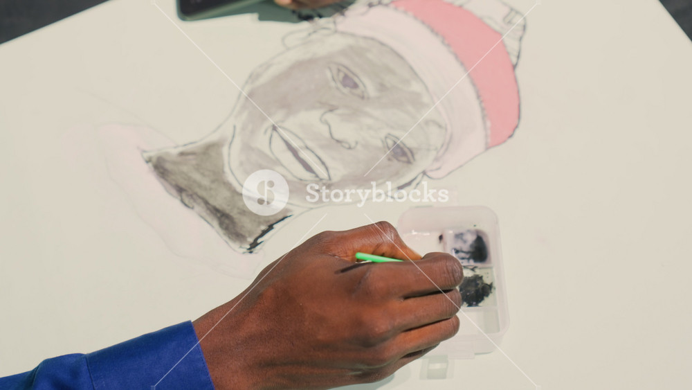 Black painting portrait with green brush, Black illustrator adds fine watercolor highlights to cheek and beanie, closeup of darkskinned