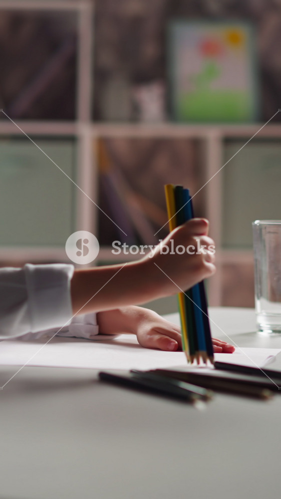Funny little child with plait takes bunch of colorful pencils to draw picture sitting at table in children classroom closeup slow motion