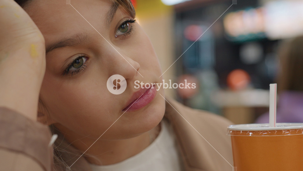 young caucasian influencer sipping orange drink in busy food hall, dreamy gaze, hand through hair, branded cup, warm bokeh lights, stylish
