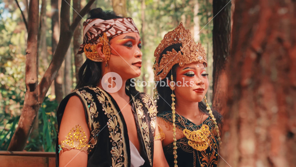 A male and female Javanese dancer in full traditional costumes and makeup share a tender embrace. The woman rests her head on his shoulder, portraying a romantic scene from Indonesian folklore.