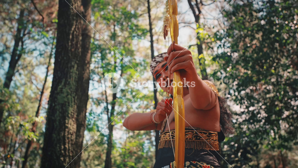A traditional Javanese male dancer, costumed as a mythological archer, stands with his golden bow in a beautiful forest clearing, embodying the spirit of Indonesian epic heroes like Arjuna.