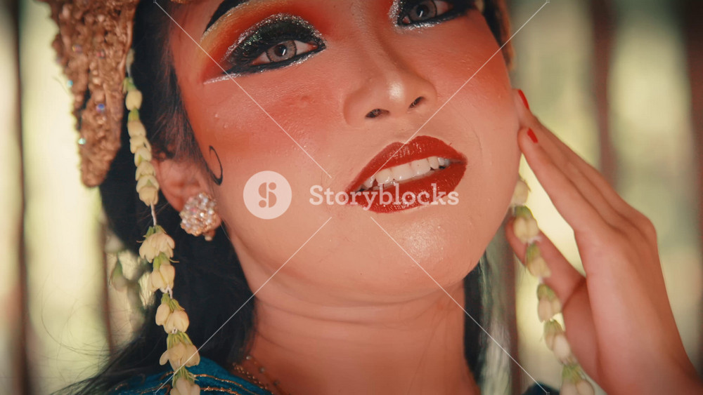 A stunning close-up of a female Javanese dancer's face. Her serene and pensive expression is highlighted by the dramatic, traditional makeup and an ornate golden headdress with jasmine flowers.