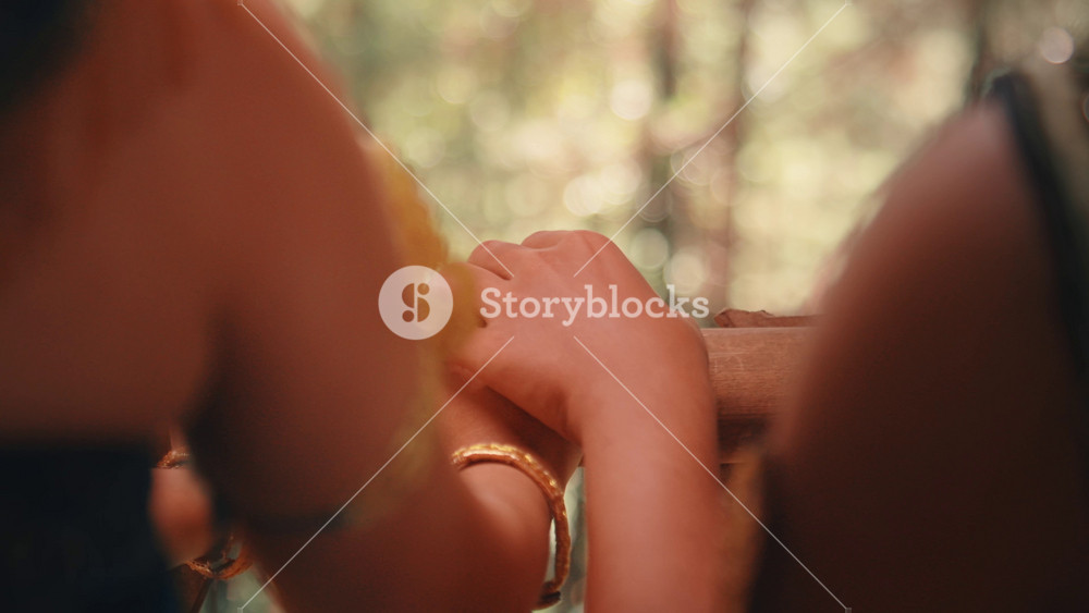 A tender close-up from behind, focusing on the hands of two lovers resting on a bamboo railing. The woman, wearing a golden bracelet, moves her hand closer to her partner's in a gentle gesture.