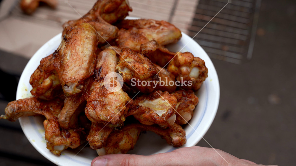 Delicious chicken frying on barbecue grill grate outdoor. Seasoning falling on fresh grilled chicken wings. Summer party food ideas. BBQ