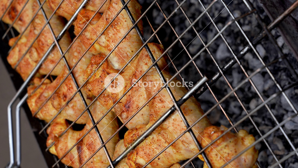 Delicious chicken frying on barbecue grill grate outdoor. Seasoning falling on fresh grilled chicken wings. Summer party food ideas. BBQ