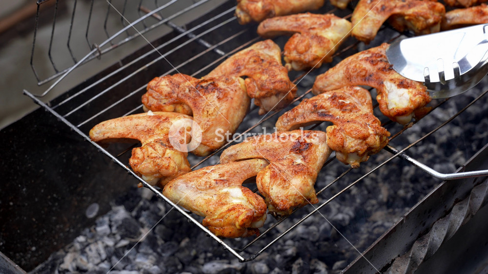 Delicious chicken frying on barbecue grill grate outdoor. Seasoning falling on fresh grilled chicken wings. Summer party food ideas. BBQ