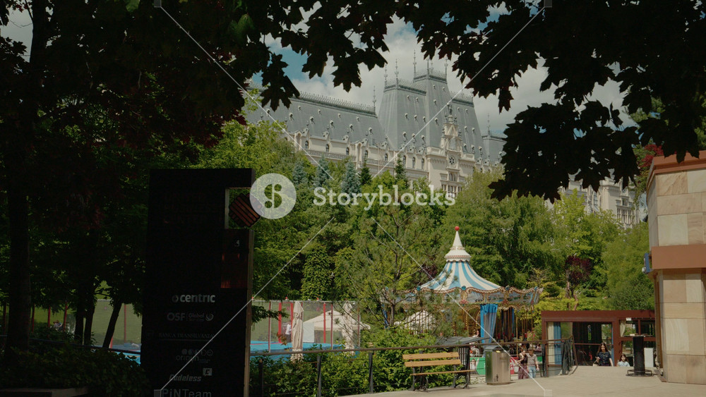 IASI, ROMANIA - June 20, 2026: People enjoy their time in the garden near the Palace of Culture in Iasi. The area features green spaces, a carousel, and pathways for strolling and relaxing.