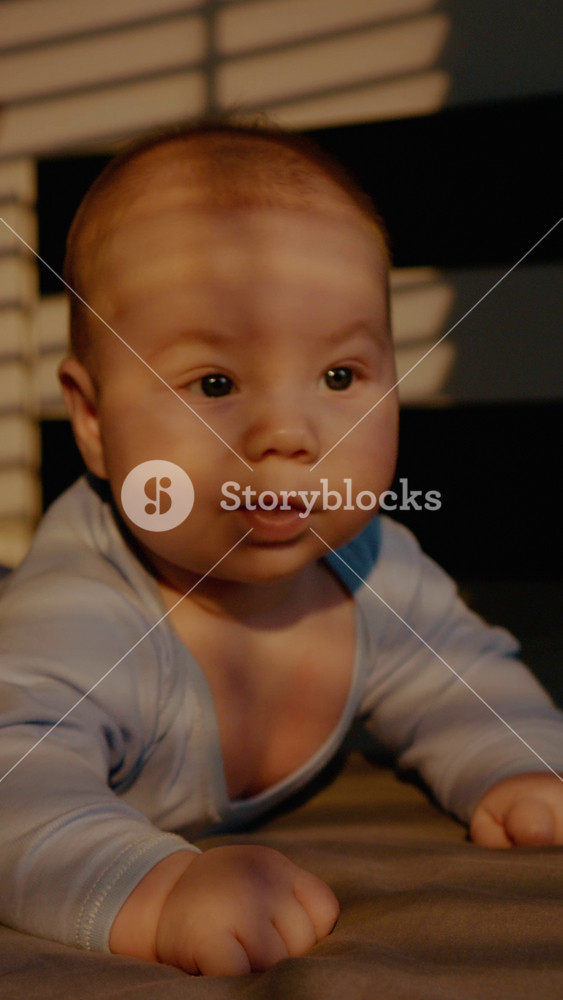 Vertical Screen: Cute baby lies on his stomach while exploring world at home environment. Concept of children health, infancy, strengthening muscles of neck and arms.