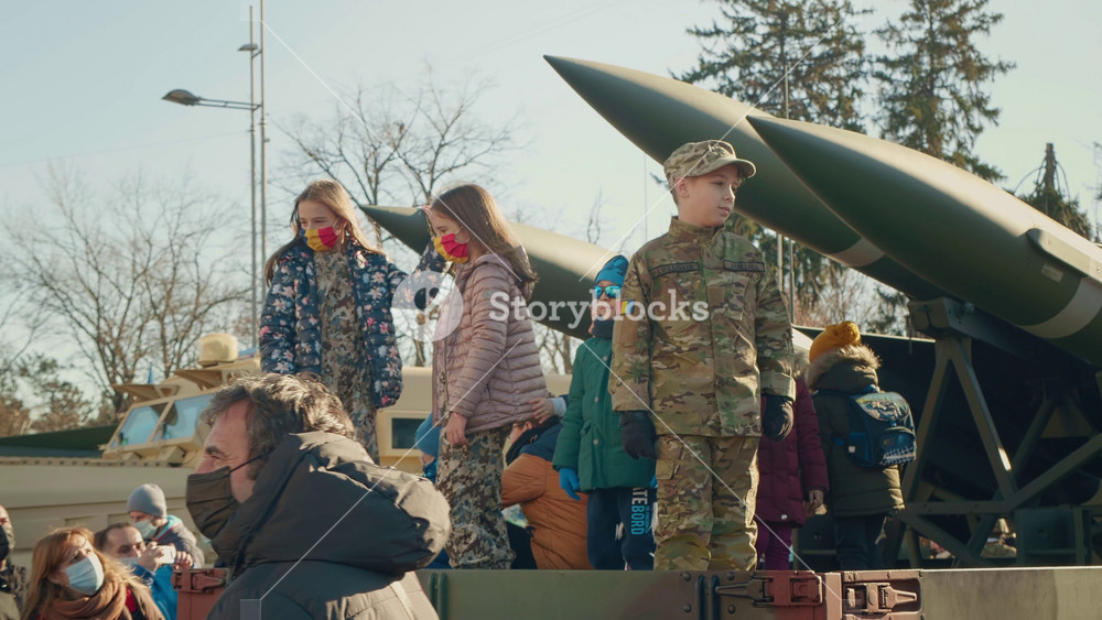 Bucharest, Romania - 1 December, 2024: Romania National Day. Children on Romanian military transport take photos with military missiles, wear masks with the Romanian flag.