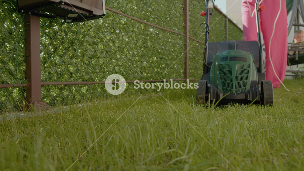 Watch as a woman expertly maneuvers an electric lawn mower to trim grass along curbs and edges in a beautifully maintained suburban yard.