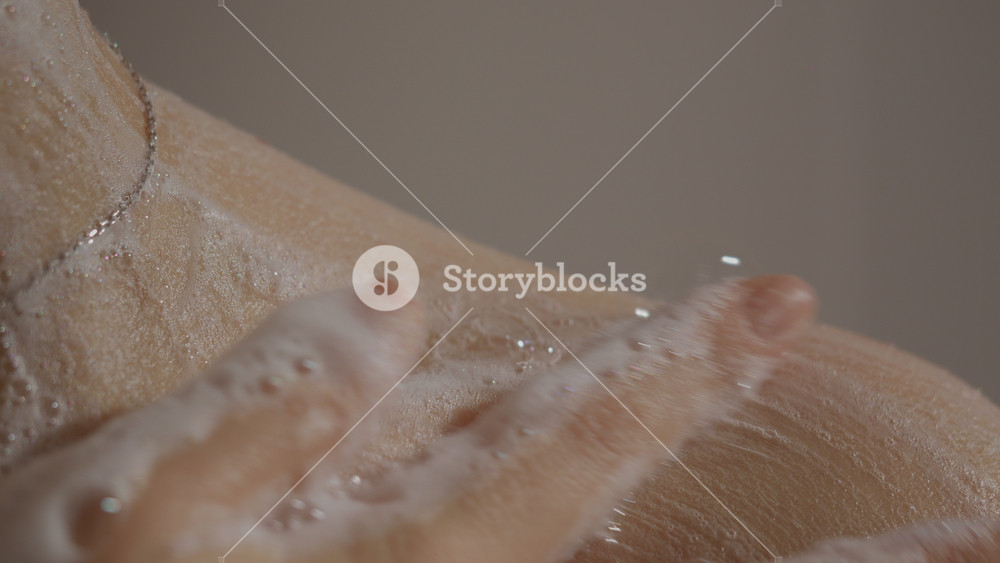 In a calming setting, a woman washes herself in the shower, carefully applying body gel to her shoulder and enjoying the soothing sensation of water and foam.