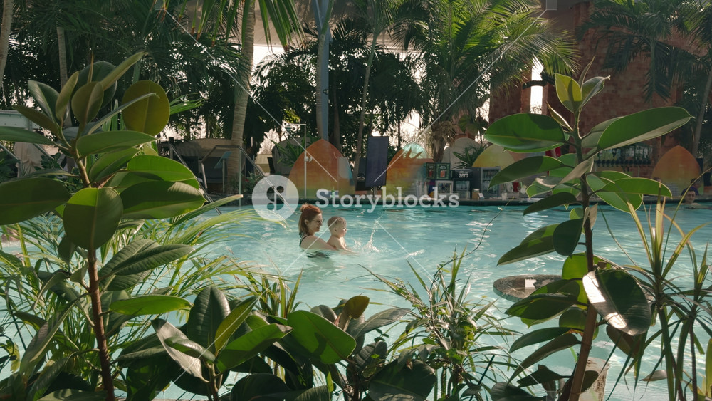 Bucharest, Romania - 2025 Feb 11: Young mother and her baby have fun together in a beautiful thermal pool, surrounded by lush palm trees. They enjoy quality family time in a relaxing environment.
