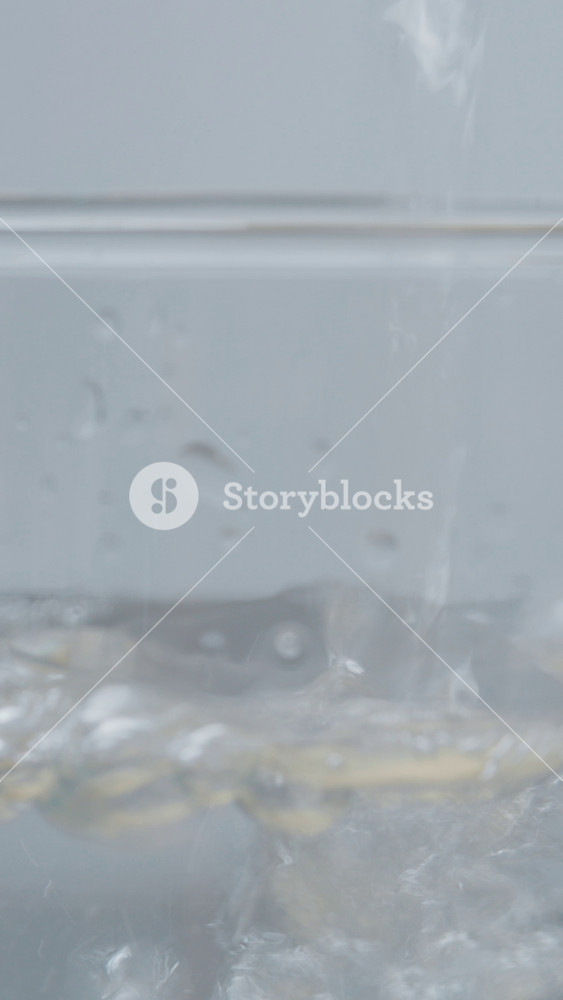 Vertical Screen: Clear water pours into a glass, filling it to the top. As the glass fills, air bubbles form and create splashes, showcasing the movement of water.