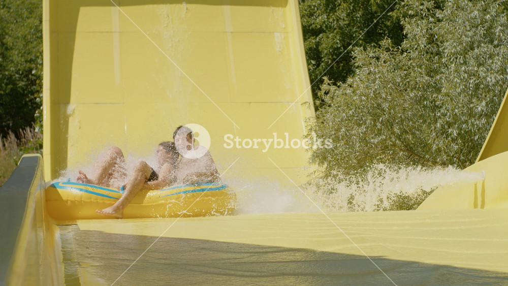 Chisinau, Republic of Moldova, - 20 August 2024: Couple roll down a yellow water slide in an aqua park. Water slide, aqua park with pool. Playground for children on summer holiday.