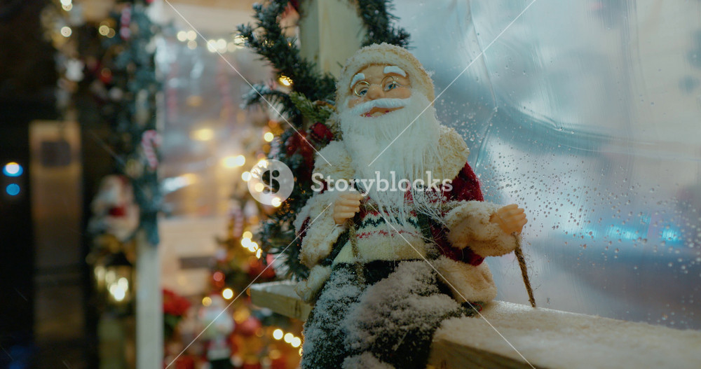 Decorations in the Christmas market, decorative Santa standing in the snow. Out of focus holiday background. Light bokeh from Xmas tree. New Year theme, background.