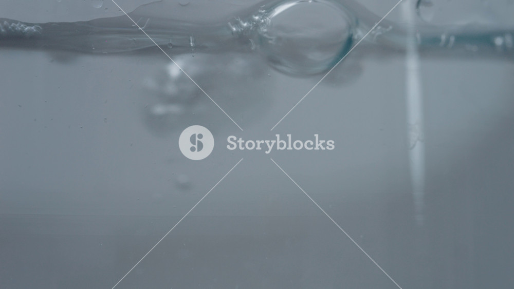 Water flows into a clear glass, creating bubbles that rise and burst as the glass fills. The close-up view highlights the movement and clarity of the water.
