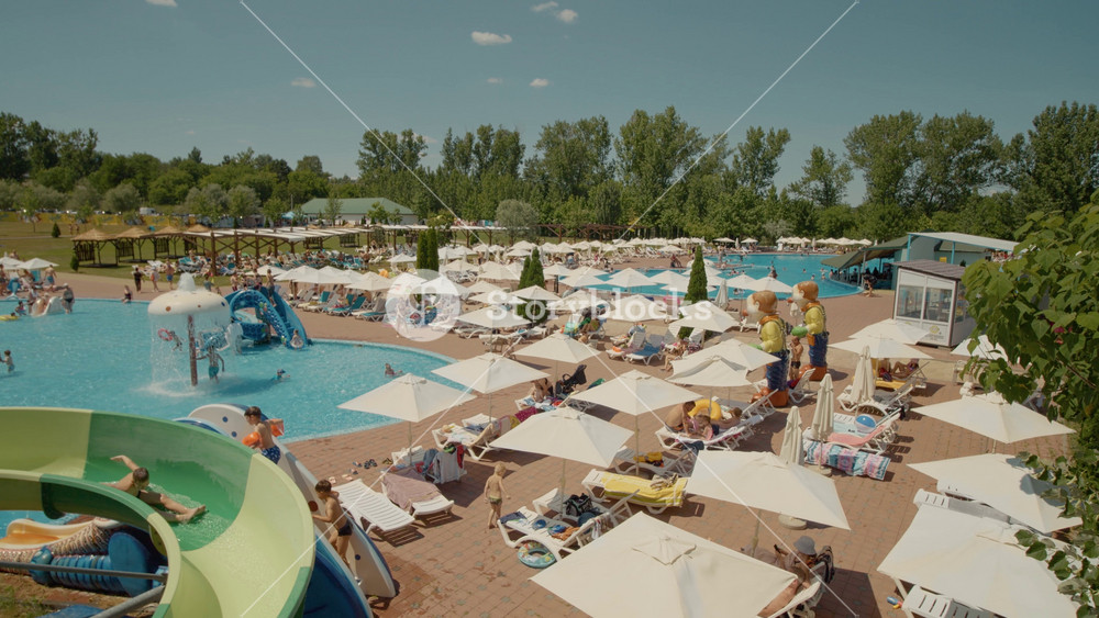 Chisinau, Republic of Moldova, - 20 August 2024: Crowd of people swimming in the outdoor pool and sunbathing on sun loungers at an Aqua Park. Playground for children on summer vacation.