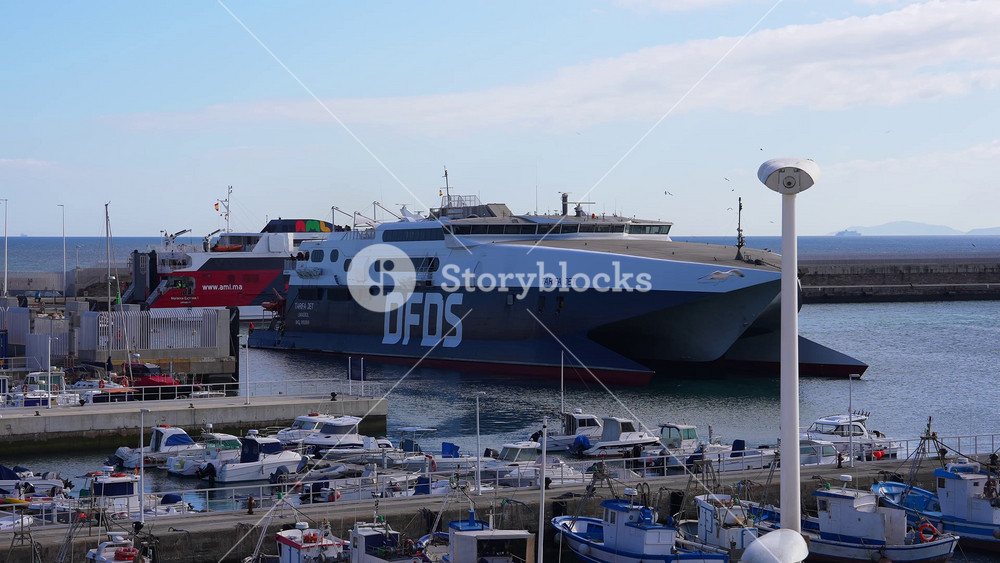 The port of Tarifa, Spain, features the DFDS ferry Tarifa Jet, smaller boats, and the Atlantic Ocean, with Morocco visible across the Strait of Gibraltar.