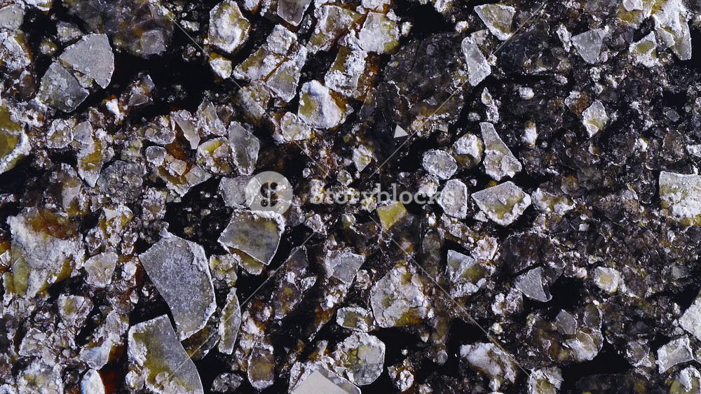 Aerial top down view shows jagged ice floes and black leads drifting near Mangalsala Lighthouse in Riga, Latvia, with snow rims and yellow brown sediment stains.