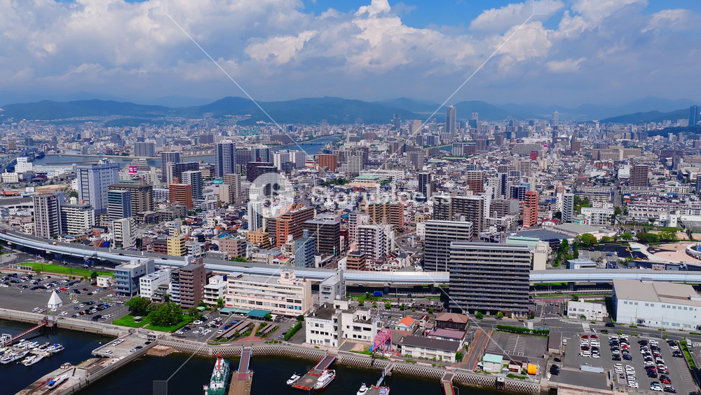 Aerial view of Hiroshima city, showcasing modern buildings, traditional structures, a marina with boats, green spaces, and distant mountains.