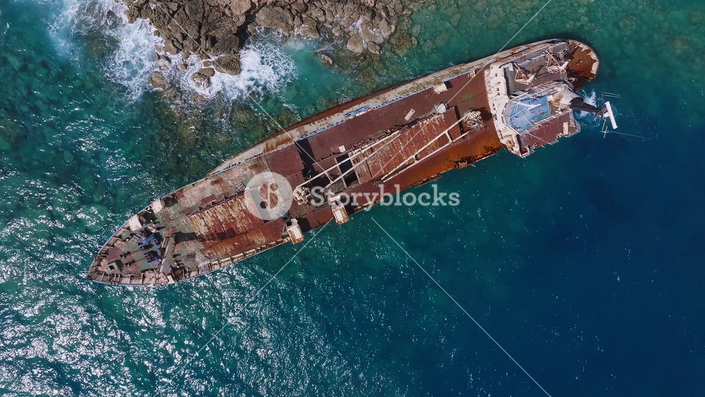 Aerial view of the Edro III shipwreck near Cyprus' rocky coast. The camera moves slowly, showcasing the rusted ship and vibrant blue waters.