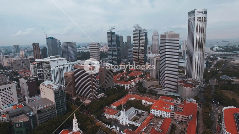 Aerial view of Singapore's skyline, showcasing modern skyscrapers, red roofed buildings, Marina Bay Sands, Swissotel The Stamford, and lush greenery.