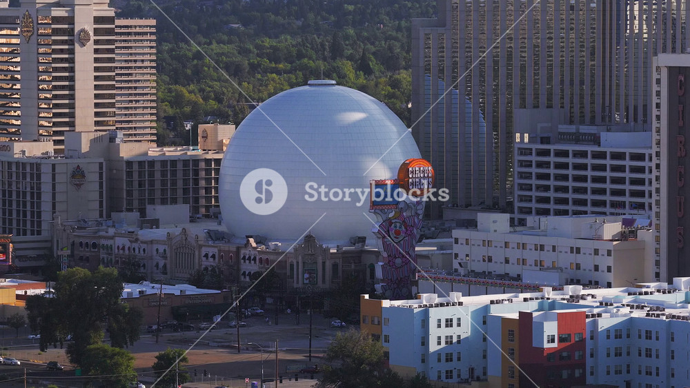 Aerial view of Reno, Nevada, at sunset, featuring the Circus Circus dome, colorful signage, high rise buildings, and lush greenery in the background.