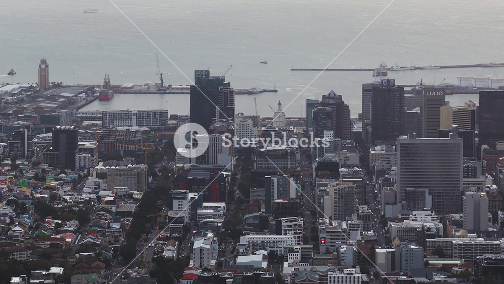 Aerial view of Cape Town, South Africa shows city center, Table Bay, V and A Waterfront, port cranes, breakwaters, storage tanks, Luno sign, and white clock tower.