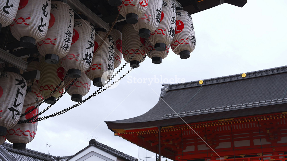 Dozens of white lanterns with black kanji and red emblems sway beside a vermilion temple gate at Senso ji in Asakusa, Tokyo, shot daylight under overcast.