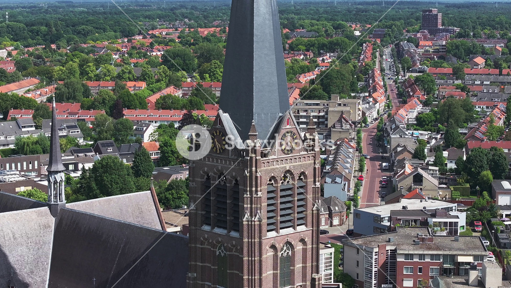 Aerial view of Eindhoven, Netherlands, highlighting the Church of St. Catherine's twin spires, clock face, and surrounding urban and green areas.