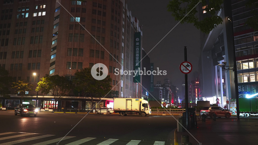 A bustling Shanghai street at night features high rise buildings, city lights, Chinese signage, and active traffic with trucks and taxis.