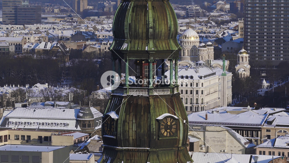 Aerial 4K over central Riga, Latvia shows St. Peter's Church tower, clock faces, visitors on the balcony, and Nativity of Christ Cathedral domes in crisp winter light.
