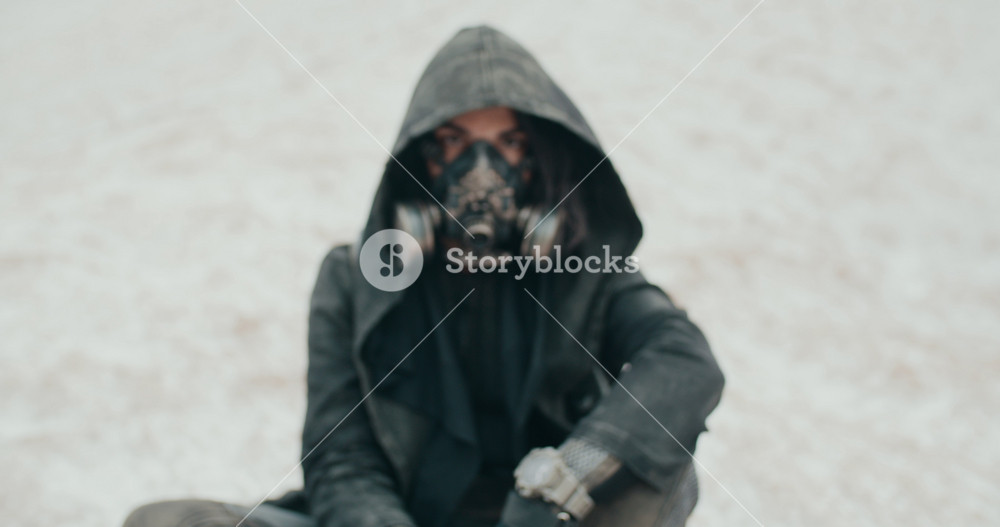Portrait post apocalyptic brunette woman wearing grunge hooded mantle protective gas mask in desert. Steampunk cyberpunk wanderer. Stalker concept, future female survivor after nuclear war