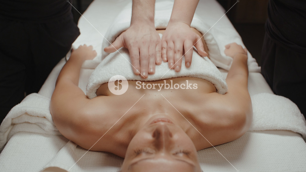 Slim brunette woman receiving health body rejuvenating massage procedure in spa center. Pair of massage therapists male and female doing light relaxing massage.