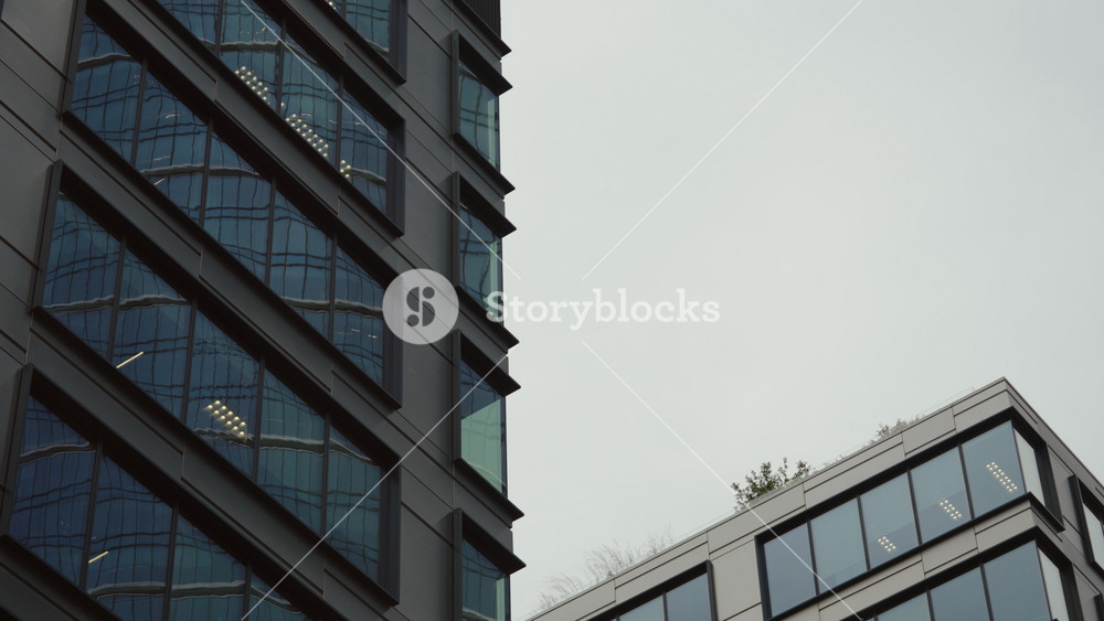 POV close-up shot from inside car driving through streets of modern city. Windshield view urban landscape, modern buildings windows glass, lighting poles and communications in slow motion, cloudy day