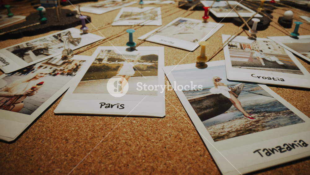 Close-up dolly shot of cork board travel world map, camera flies over many printed photographs, young woman and her travel destinations. Lot of colorful pins connected with thread, female photo images