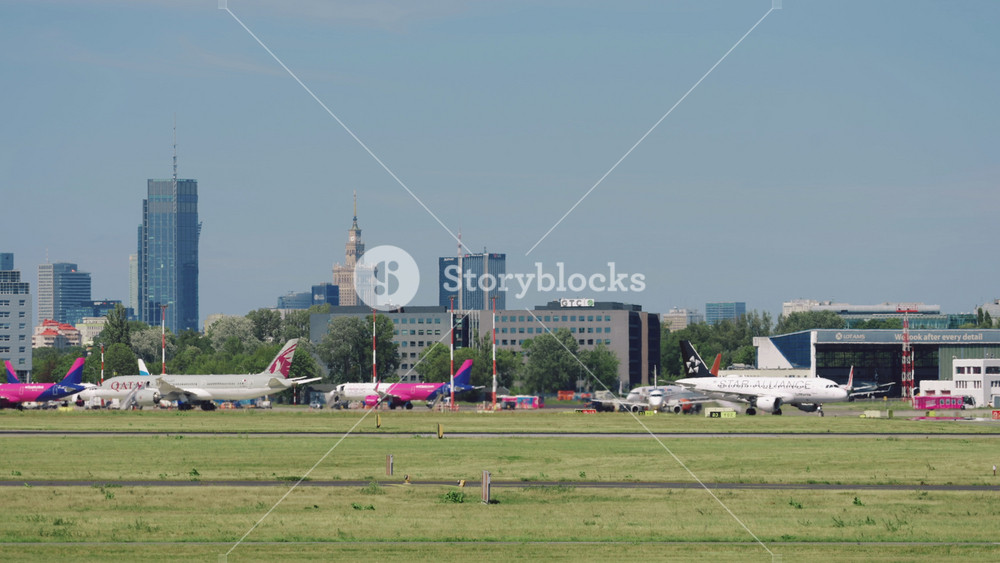 Warsaw, Poland - 03.07.2024: passenger airplanes taxiing on airfield runway slow motion. Commercial aircrafts in Chopin international airport on warm sunny day. City on horizon, downtown skyscrapers