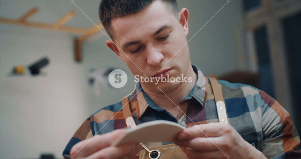 Portrait of handsome male carpenter sanding wooden toy with sandpaper in workshop. Attractive man working with craft bird wing detail made of wood polishing surface. Small business and hobby concept